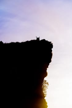 Black silhouette on sky background of two tourist standing arms outstretched happy with success on peak mountain near the cliff during sunrise at Phu Chi Fa Viewpoint, Chiang Rai, Thailand