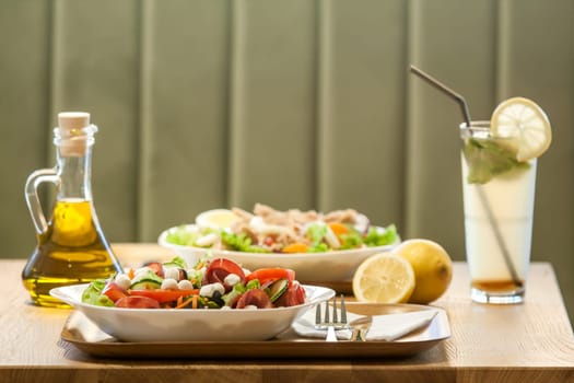 Two salads with ham, meat, tomatoes, mozzarella, lemon juice and olive oil bottle