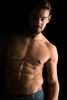Handsome young man, shirtless, with great body posing over a black background