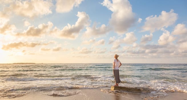 Relaxed woman enjoying sun, freedom and life an beautiful beach in sunset. Young lady feeling free, relaxed and happy. Concept of vacations, freedom, happiness, enjoyment and well being.
