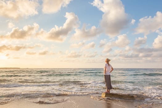 Relaxed woman enjoying sun, freedom and life an beautiful beach in sunset. Young lady feeling free, relaxed and happy. Concept of vacations, freedom, happiness, enjoyment and well being.