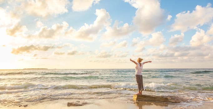 Relaxed woman enjoying sun, freedom and life an beautiful beach in sunset. Young lady feeling free, relaxed and happy. Concept of vacations, freedom, happiness, enjoyment and well being.