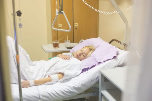 Bedridden female patient lying in hospital bed, recovering after surgery.