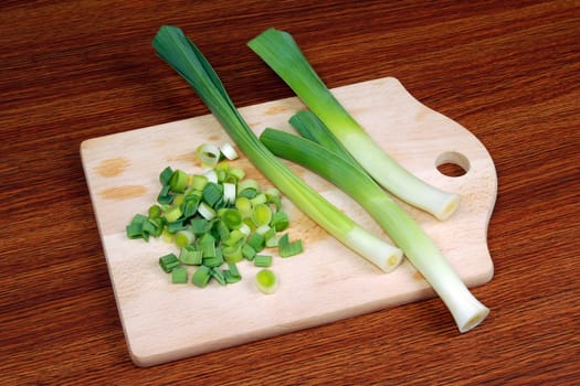 Leeks and slices are on cutting board on wooden table.