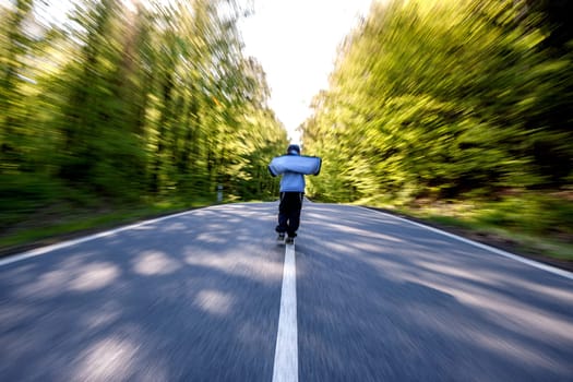 Panning shot of boy walking through a road in the middle of a forest