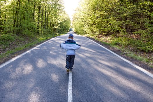 Panning shot of boy walking through a road in the middle of a forest