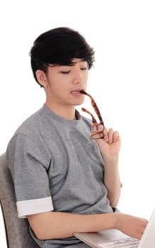 A young Asian man sitting and working hart on his laptop to solve the.problem, with glasses in his mouth, isolated for white background..