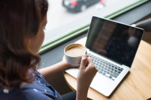 Beautiful cute asian young businesswoman in the cafe, using laptop and drinking coffee smiling