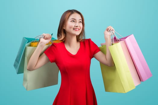 Beautiful young asian woman with colored shopping bags over blue background