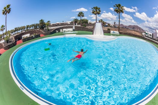 teenage BOY HAS FUN SWIMMING ON A SURF BOARD IN THE POOL