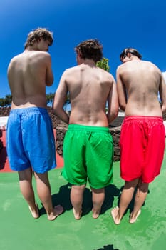 three teenage boys stand close together iin the pool area