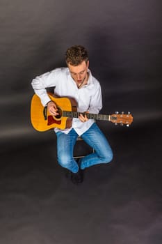 teenage guitar player sits on a chair and plays guitar