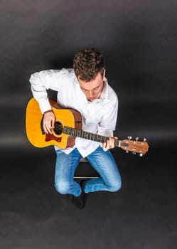 teenage guitar player sits on a chair and plays guitar