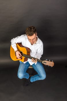 teenage guitar player sits on a chair and plays guitar