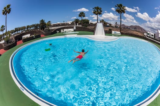 teenage BOY HAS FUN SWIMMING ON A SURF BOARD IN THE POOL