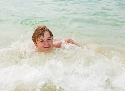 young happy boy with brown hair enjoys swimming in the beautiful sea
