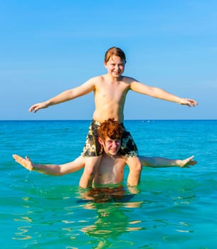brothers are enjoying the clear warm water at the beautiful beach and playing pickaback