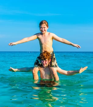 brothers are enjoying the clear warm water at the beautiful beach and playing pickaback
