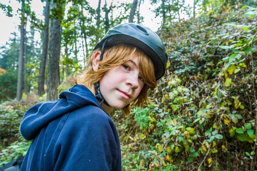 portrait of young teenage boy in forest with bike helmet