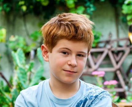 portrait of cute smiling boy with red hair sitting in the garden