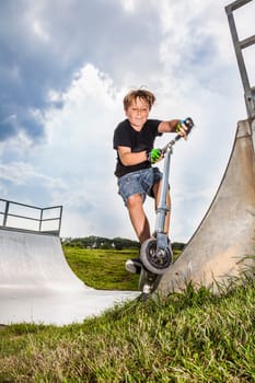 boy enjoys riding his scooter in the skate park