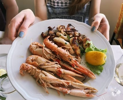 female hands keeping plate with shrimp squids and lemon