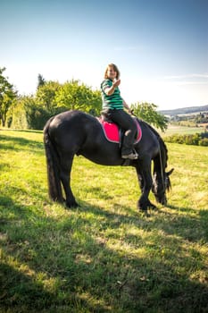 Young rider with her Frisian horse in summer in nature