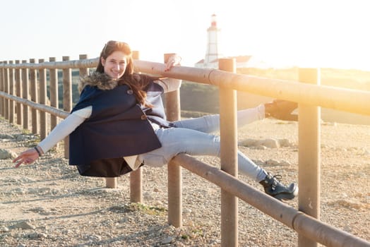 Beautiful happy young girl posing outdoors at sunset near a lighthouse