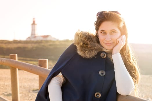 Beautiful happy young girl posing outdoors at sunset near a lighthouse