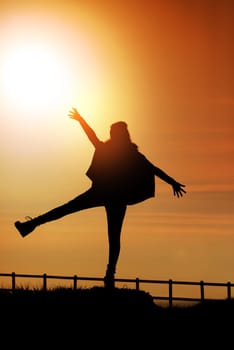 Girl in silhouette over a fence at sunset