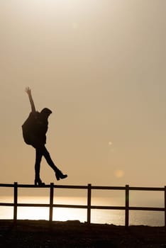 Girl in silhouette over a fence at sunset