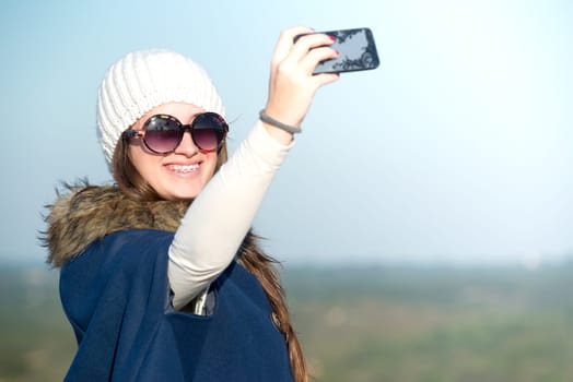 Beautiful happy young girl posing outdoors with phone taking a selfie