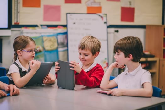 Table of primary school students in a classroom are using digital tablets to work on.
