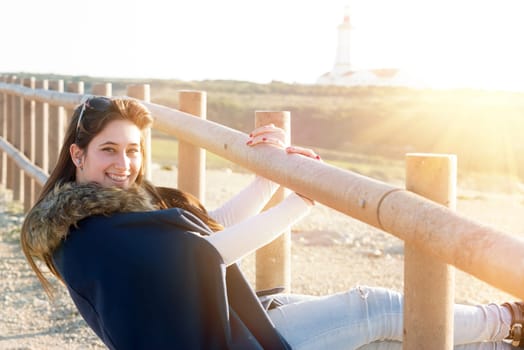Beautiful happy young girl posing outdoors at sunset near a lighthouse