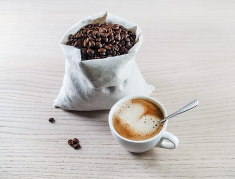 Espresso cup and coffee beans in a canvas bag against black wooden table background.