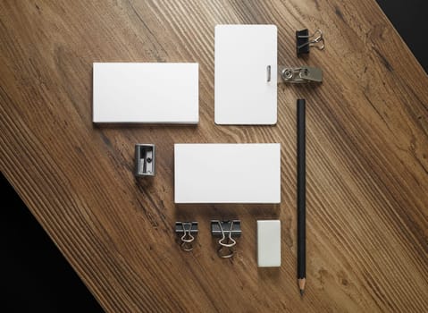 Photo of blank business cards, pencil, eraser, badge and sharpener on wooden table background. Blank stationery set. Mockup for your design. Responsive design template. Top view.