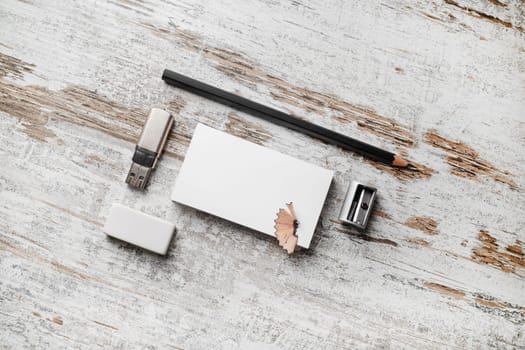 Photo of blank business cards, pencil, eraser, flash drive and sharpener on vintage wooden table background. Responsive design mockup. Mock-up for branding identity.