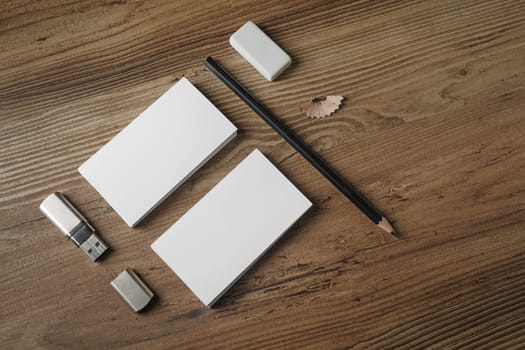 Photo of blank stationery set. Bank business cards, pencil, eraser and flash drive on wood table background. Responsive design mockup. Top view.
