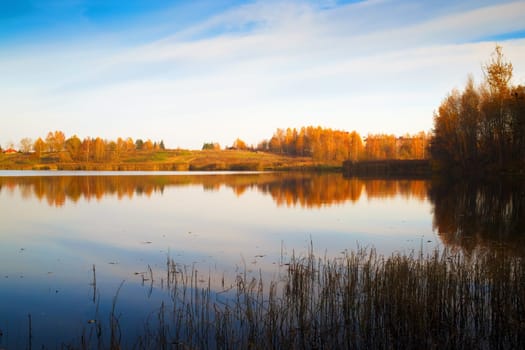 Picturesque autumn landscape. Lake with thickets of trees along the banks and blue sky.