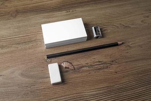 Photo of blank business cards, pencil, eraser and sharpener on wooden background. ID template. Mockup for branding identity for designers. Top view.