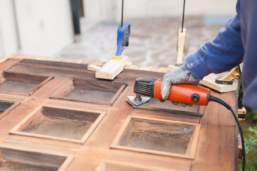 Carpenter at work with angular Sander. Maintenance and restoration of an old wooden door.