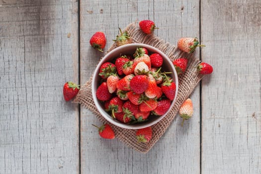 Ripe trawberries in bowl on the old wooden floor.