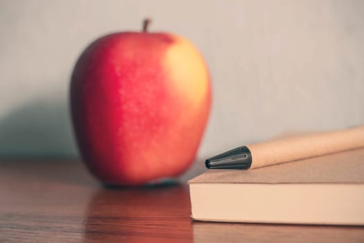 Pencil and notebook with apple on the desk.
