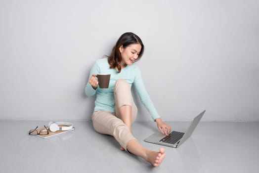 Happy casual beautiful asian woman working on a laptop sitting on floor at home.