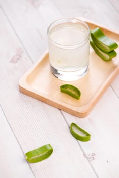 Glass of aloe vera juice with fresh leaves on a wooden table