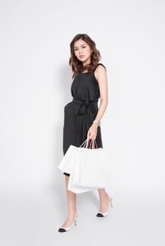 Beautiful asian woman wearing black dress with shopping bag standing over white.