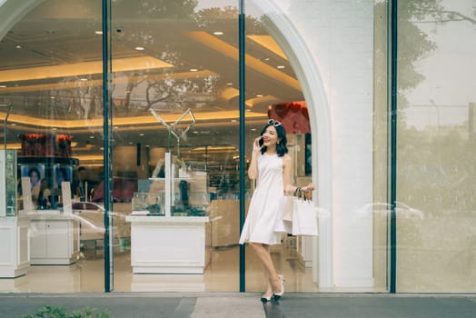 Beautiful asian girl with shopping bags listening to mobile phone standing outside the mall