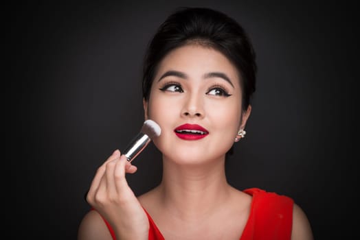 Cosmetic powder brush. Asian woman applying blusher on her cheeks with perfect make-up and red lips