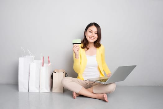 Young asian woman shopping online at home sitting besides row of shopping bags