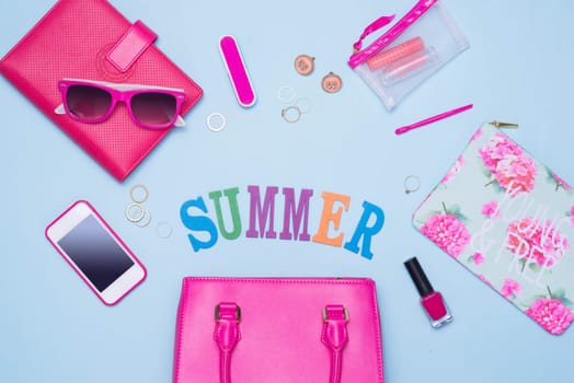 Summer concept. Pink handbag with accessories on light blue background